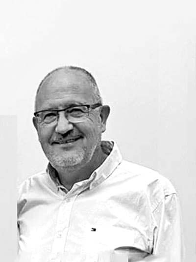 Hombre sonriente con gafas y camisa blanca.